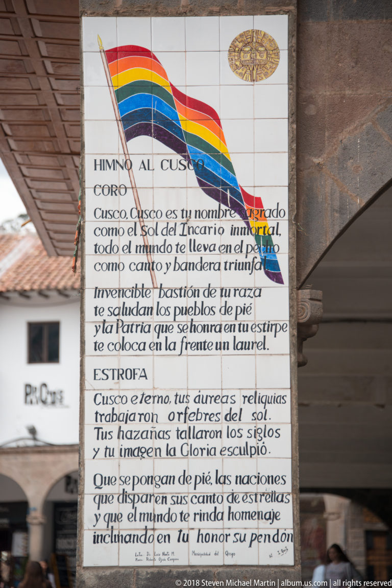 Tiled panel titled “Himno al Cusco” with Spanish verses beneath a rainbow-striped banner and gold emblem.