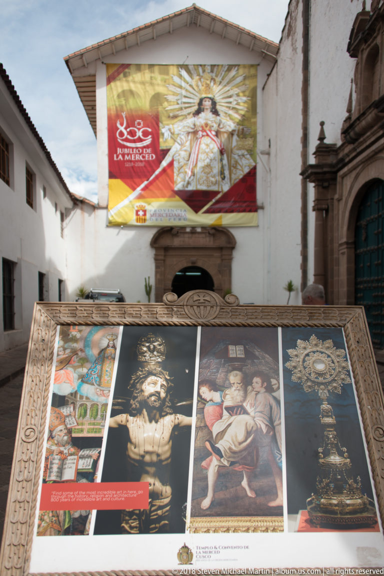 Courtyard exhibition panels reproduce colonial religious artworks beside a carved stone doorway.