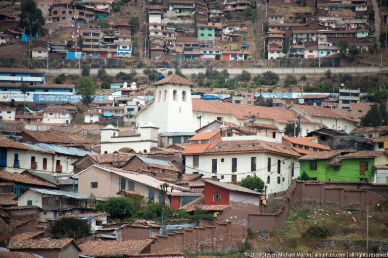 White church tower among red-tile roofs with dense hillside housing rising behind.