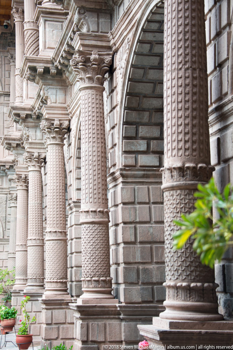 Close oblique view of richly carved stone columns and rounded arches along a cloister.