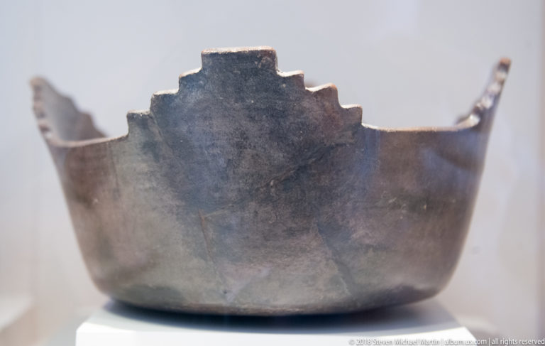 Dark gray ceramic bowl with plain curved body and a stepped, angular crest rising from one side of the rim.