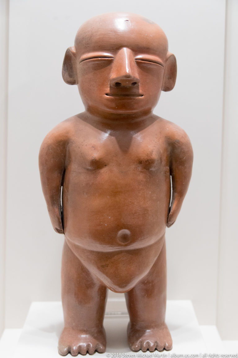 Virú sculptural ceramic jug modeled as a semi-nude standing male figure with detailed face, hands, and torso.