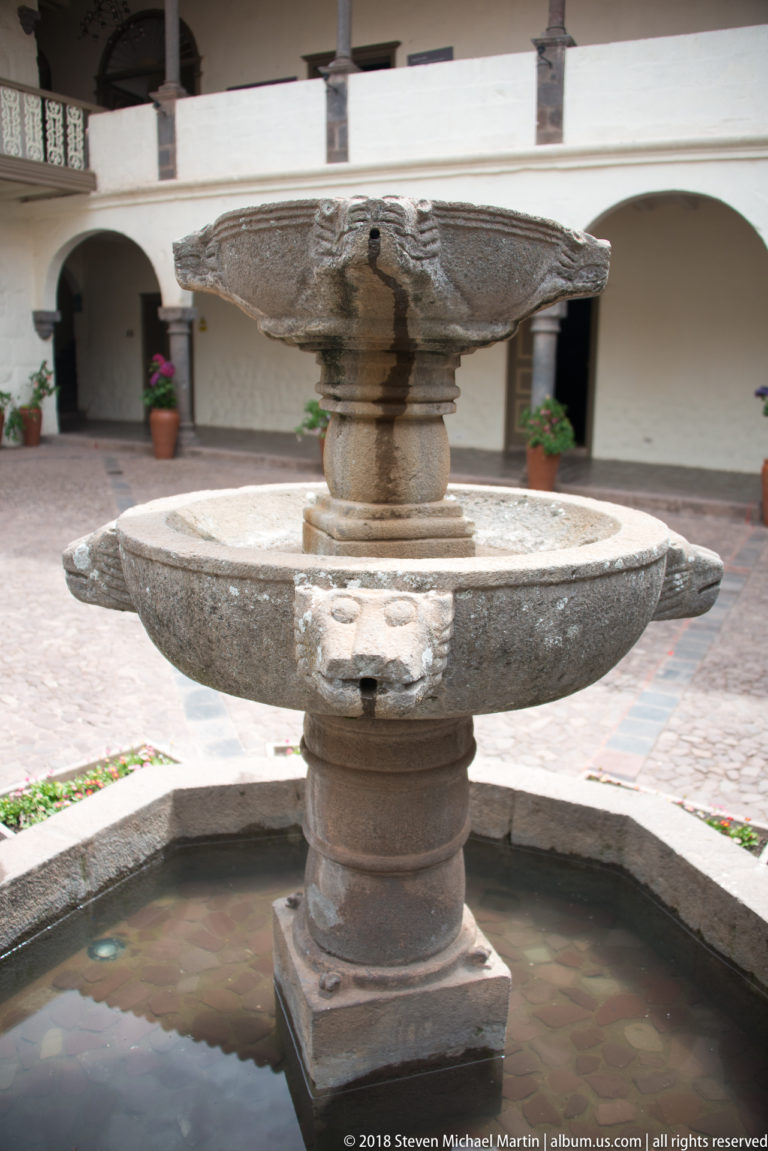 Carved stone courtyard fountain with broad circular basin, central pedestal, face-shaped spout, upper bowl, and octagonal pool.