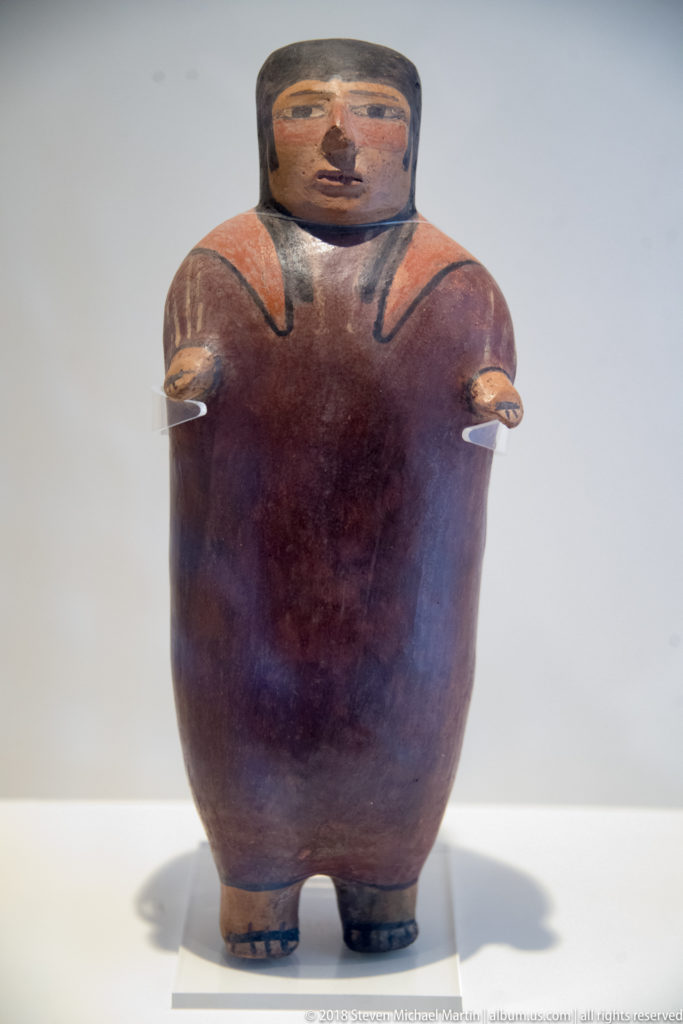 Nasca stout standing ceramic figure with short feet, outstretched arms, square head, and dark painted facial and shoulder details.