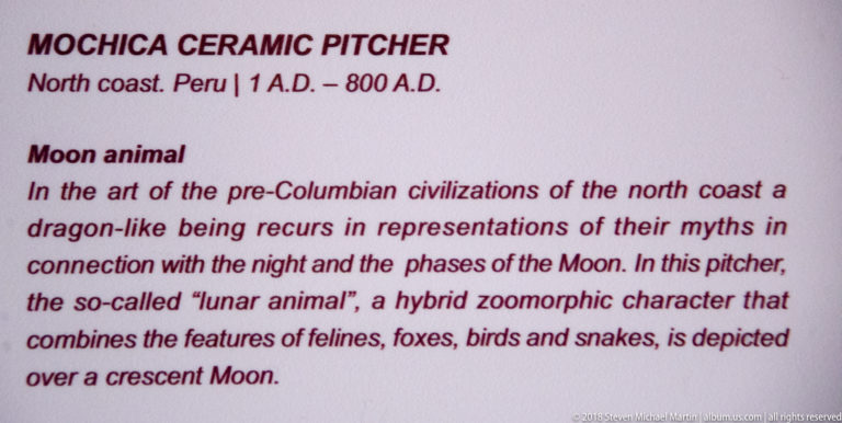 Close view of a museum label for a north-coast ceramic pitcher describing a hybrid lunar animal over a crescent moon.