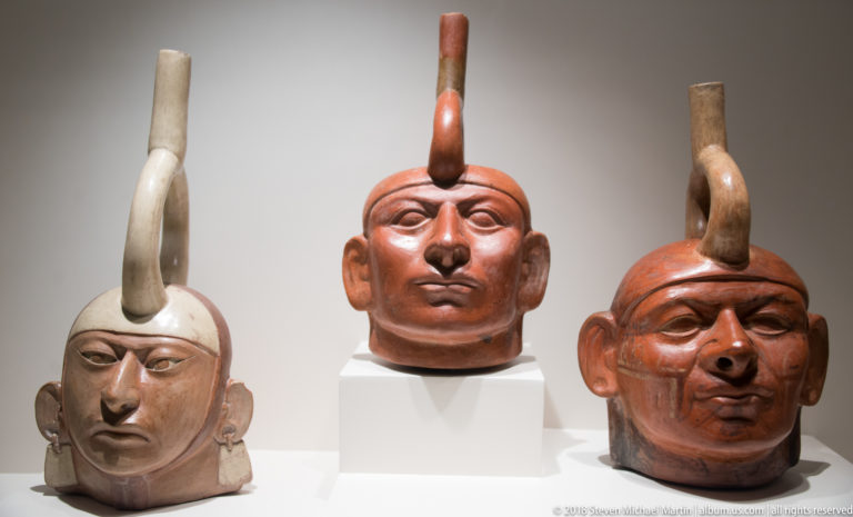 Three Moche portrait-head ceramic vessels with individualized male faces and tall spout elements rising from the tops of the heads.