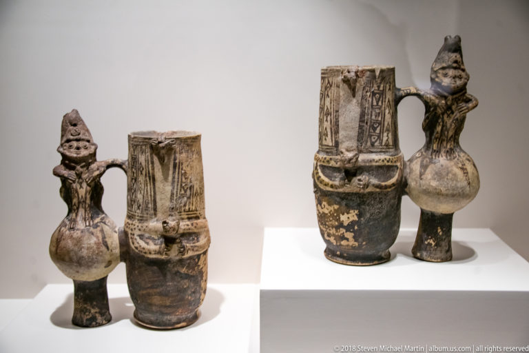 Two pairs of pre-Columbian ceramic vessels combining tall patterned cylinders with smaller modeled human figures and connecting handles.