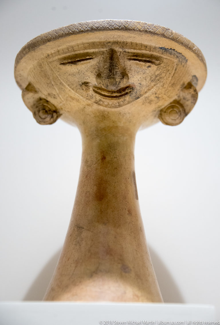 Pre-Columbian ceramic pedestal vessel with tall flaring base, broad shallow rim, and small modeled details beneath the edge.