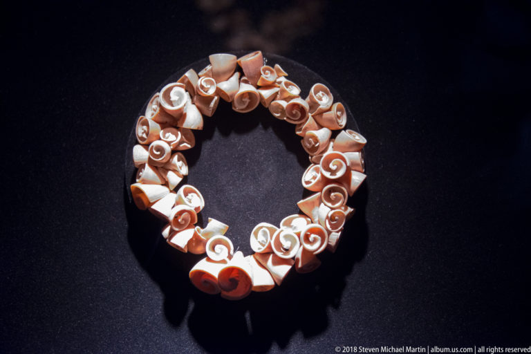 Circular necklace of many small cream and orange shell pieces, each showing a natural spiral interior.