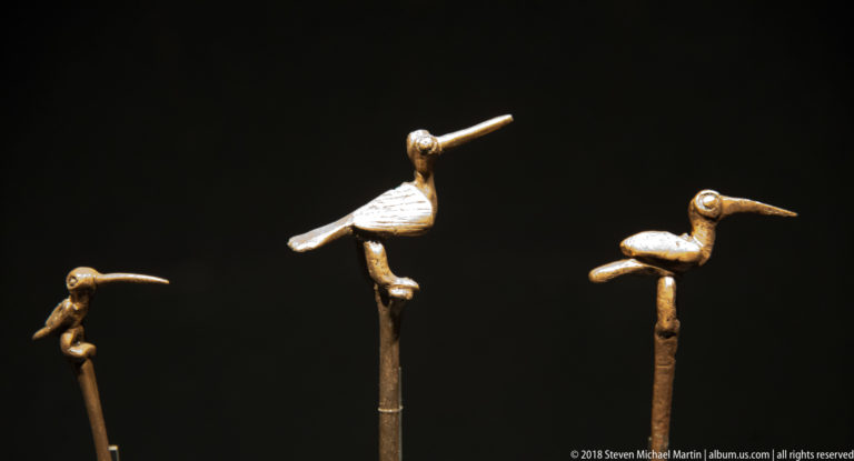 Three slender pins topped with small metal birds in varied poses, including one bird with an outstretched wing.