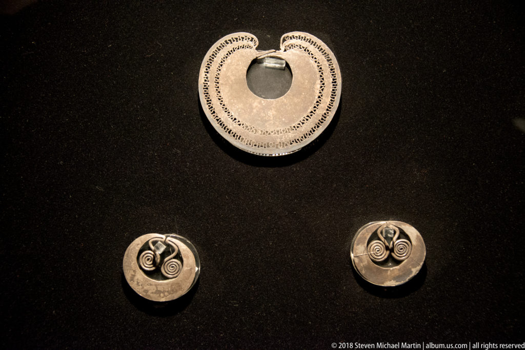 Three round silver-colored ornaments: one larger pierced disc above two smaller discs with raised paired spiral motifs.