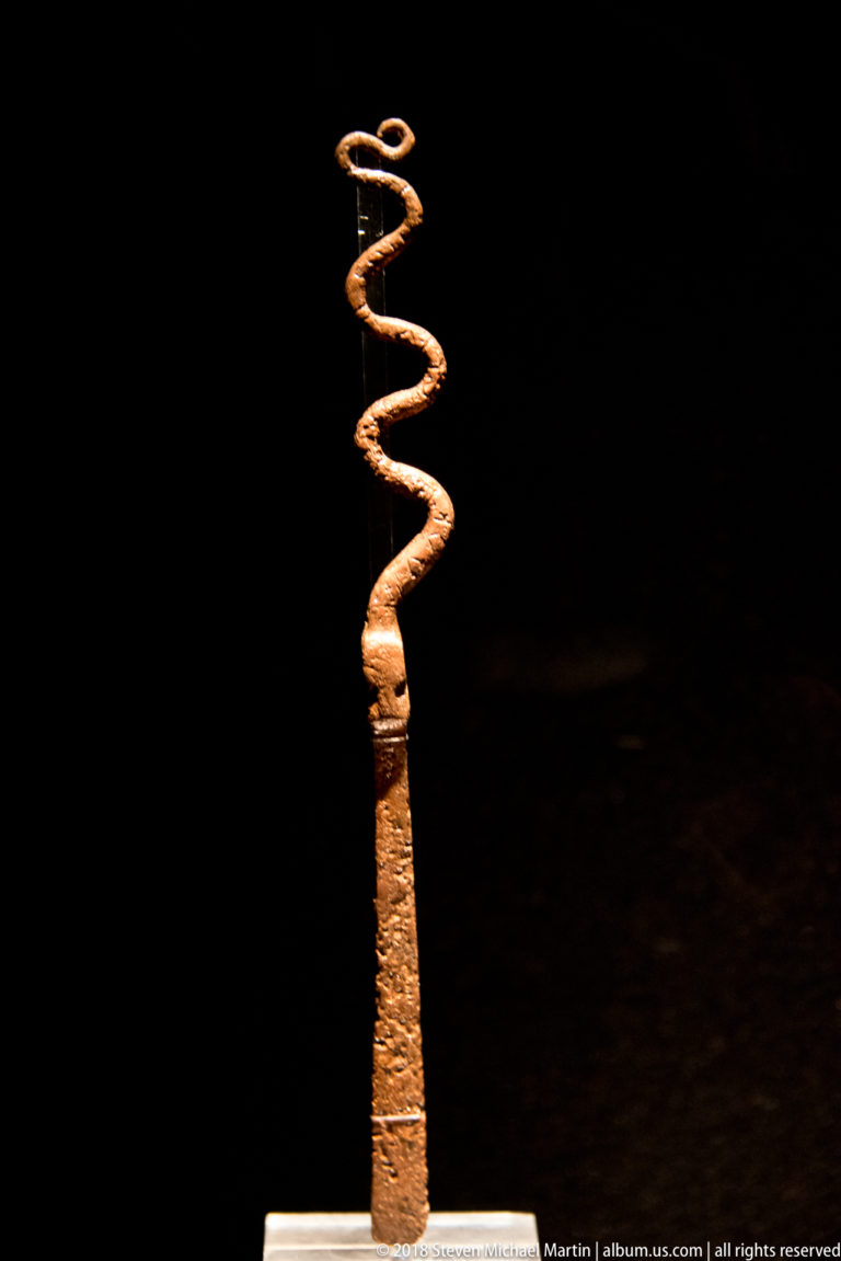 Long slender pre-Columbian metal pin with a narrow shaft and an open spiral coil forming the upper finial.