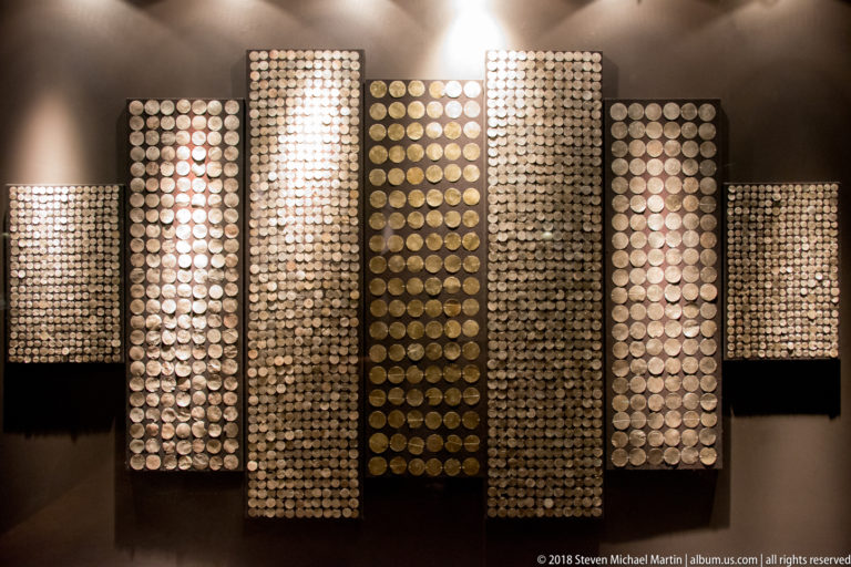 Several vertical rectangular panels densely covered with aligned rows of small circular metal discs in silver and gold tones.