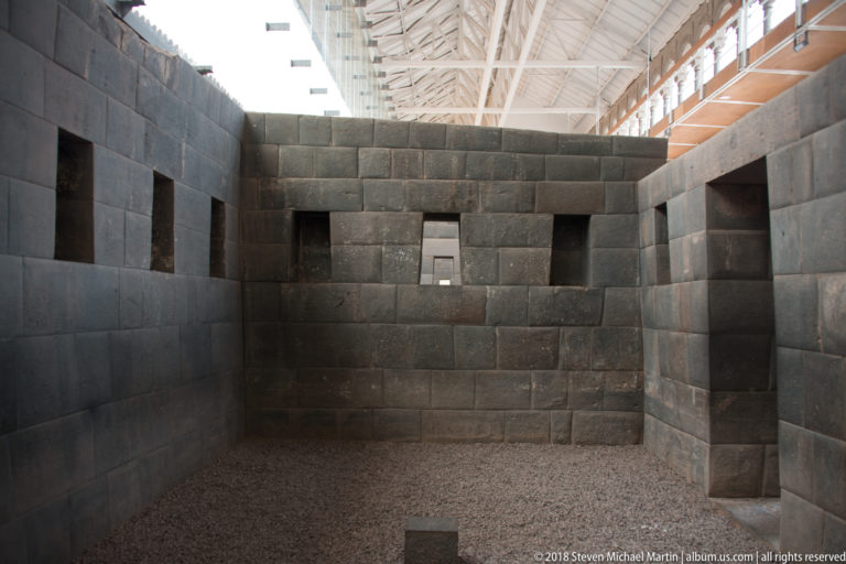 Roofed Inca stone chamber with wall niches and a centered doorway aligned to another opening beyond.