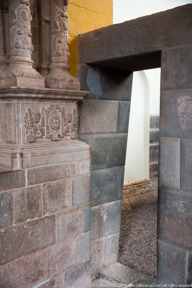 Trapezoidal Inca stone doorway beside an ornate carved stone architectural element inside the Qorikancha complex.