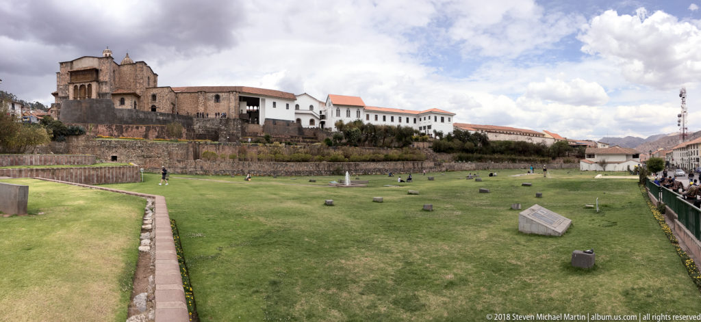 Wide lawn and stone terraces below the Santo Domingo complex at Qorikancha, with scattered stone elements in the grass.