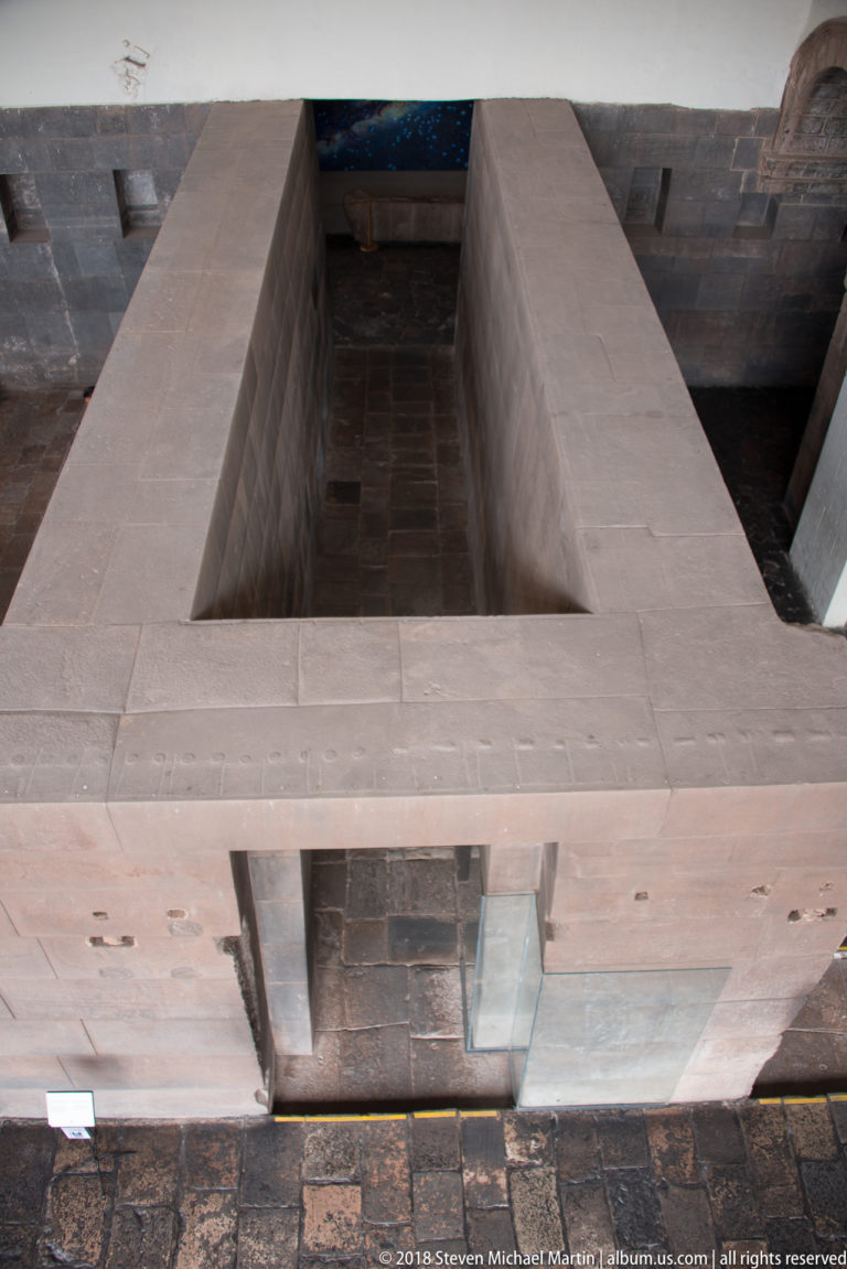 Centered view through a trapezoidal Inca doorway into a dark stone chamber with small wall niches.