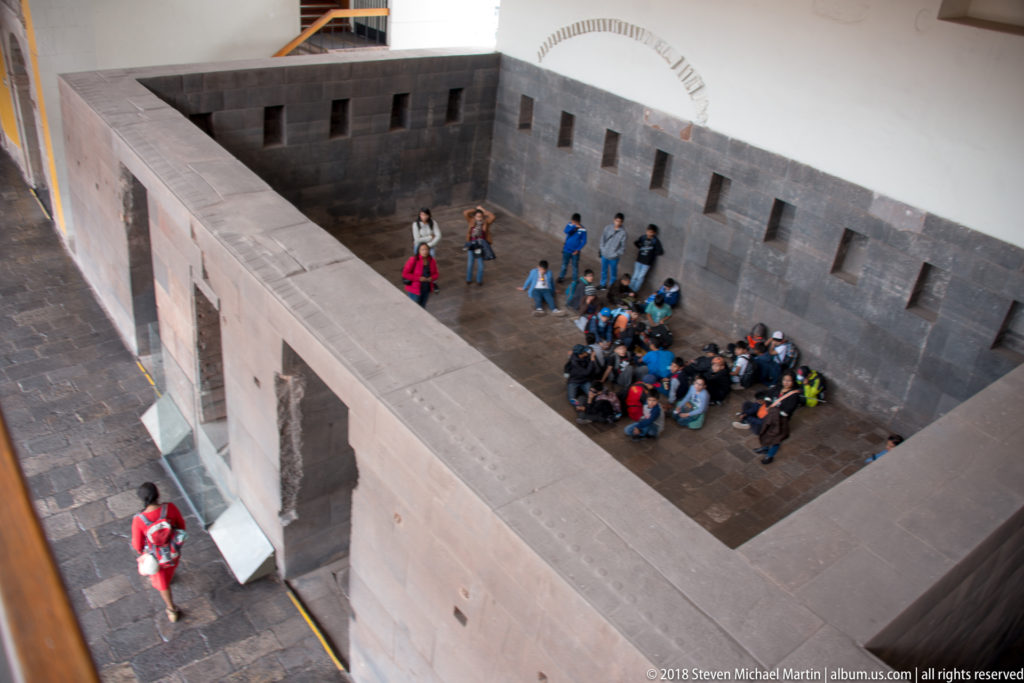 Visitors gathered beside dark Inca stone walls and niches inside the Qorikancha archaeological area.