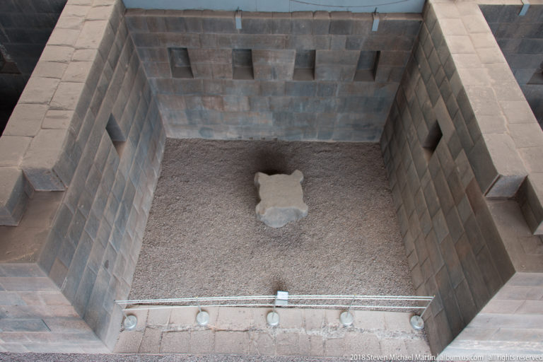 Top-down view into a rectangular Inca stone chamber with trapezoidal wall niches and a gravel floor.