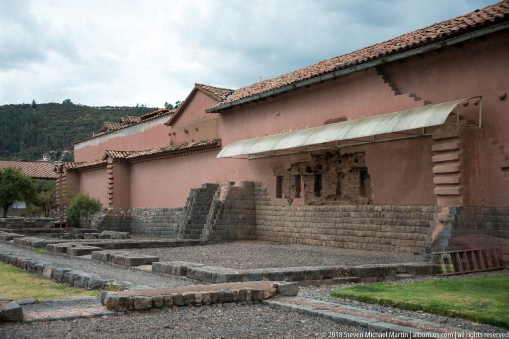 Low archaeological stone walls beside pink colonial buildings built over darker Inca masonry bases.