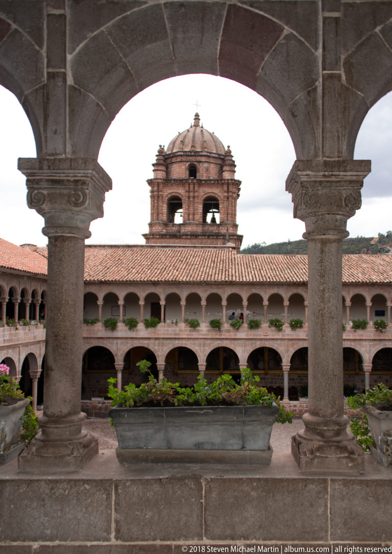 Stone arch framing a two-story cloister arcade and domed bell tower inside the Santo Domingo complex.