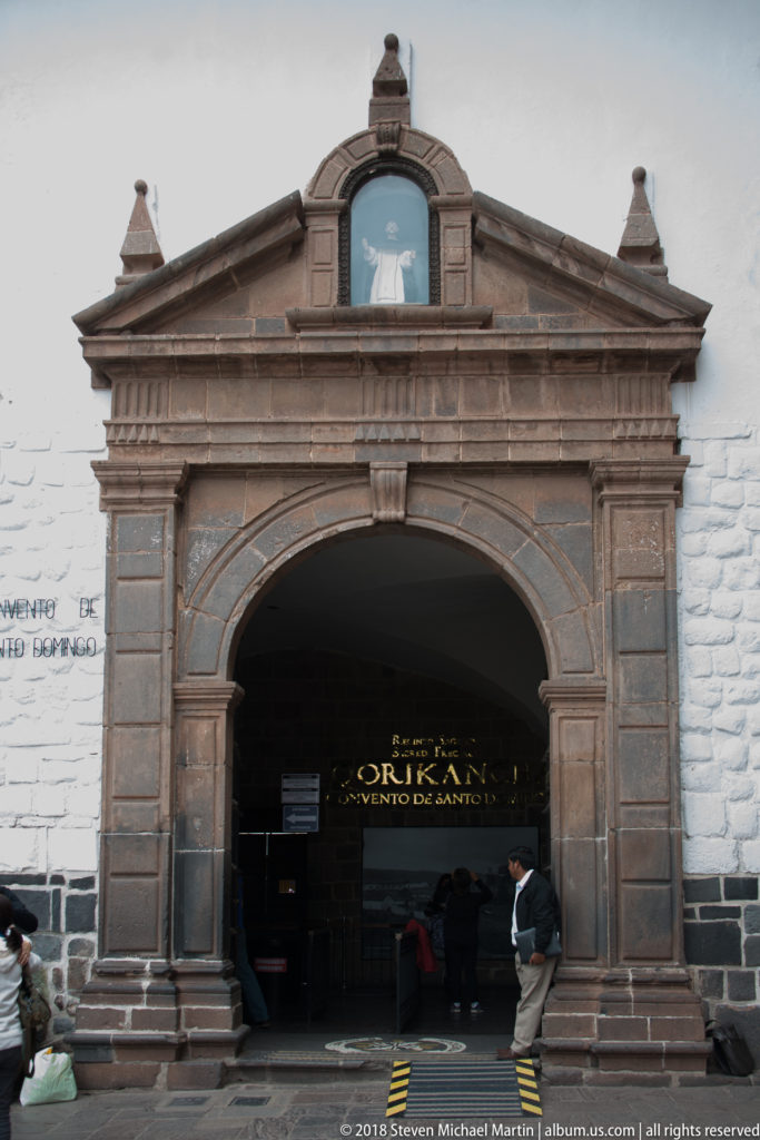 Large classical stone entrance portal to Qorikancha and the Convent of Santo Domingo, with visitors entering beneath the arch.