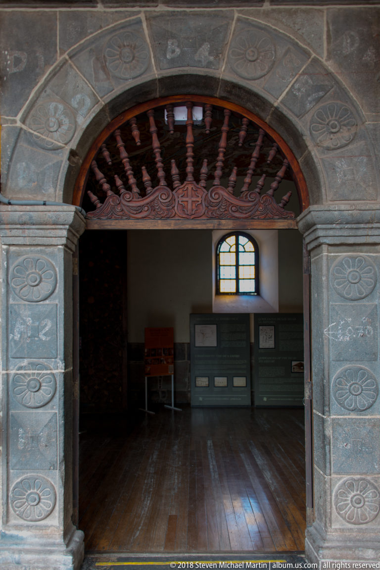 Decorated stone arched doorway with circular motifs and a dark wooden fanlight opening into an interior room.