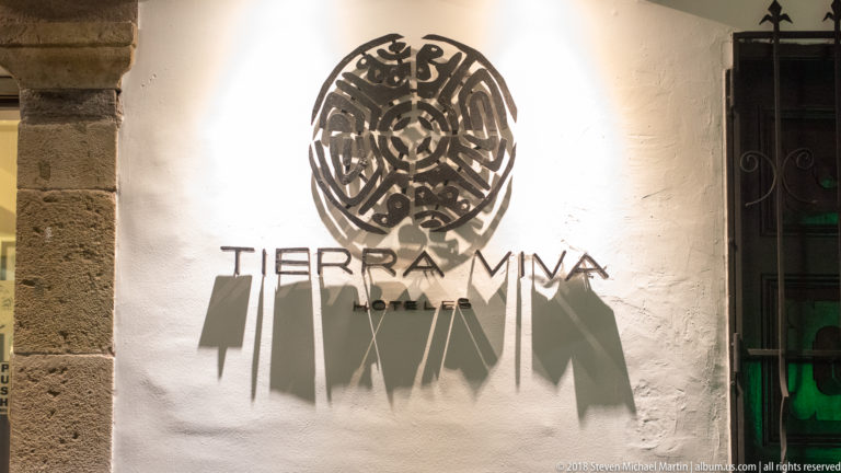 Illuminated Tierra Mía wall sign casting long shadows across white stucco at night.
