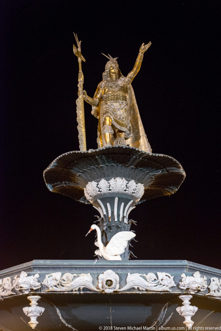 Gilded Pachacuti statue standing above the upper basin of Cusco’s Plaza de Armas fountain at night.