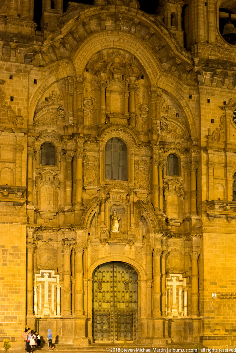 Floodlit central façade of the Church of the Society of Jesus with ornate portal, columns, niches, and upper window.