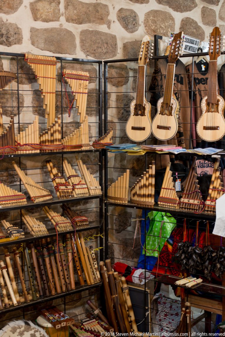 Market shelves filled with panpipes, flutes, and small guitar-like stringed instruments in Cusco.