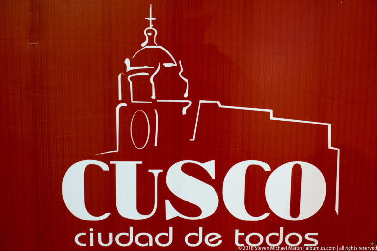 Red sign with white church outline and large text reading “CUSCO ciudad de todos.”