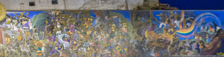 Distorted nighttime reflection of Cusco street lights, people, and colorful urban forms across a rippling reflective surface.