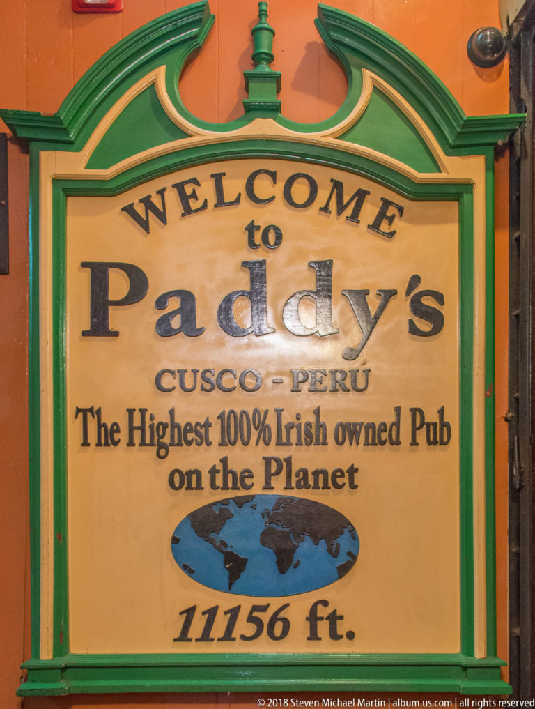 Green-framed Paddy’s Irish Pub sign in Cusco stating an elevation of 11,156 feet on an orange wall.