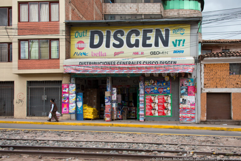 DISGEN Distribuciones Generales Cusco storefront packed with sacks and packaged goods behind railway tracks.