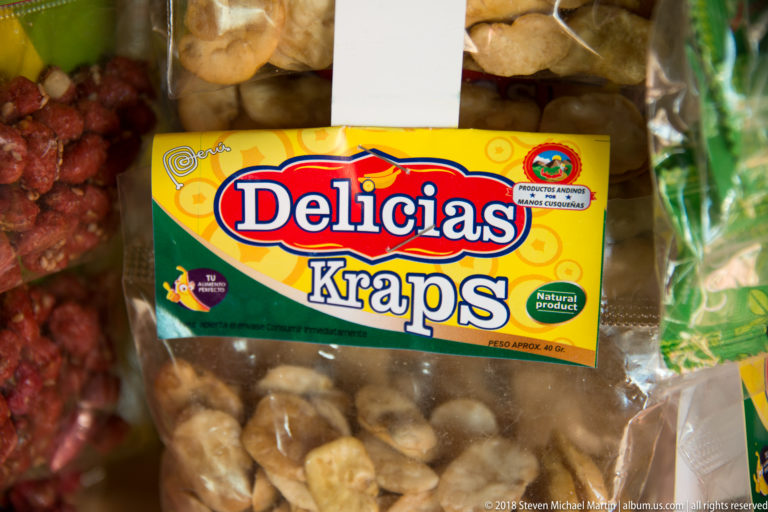Colorful Delicias Kraps package resting among clear bags of assorted snack foods at a market display.