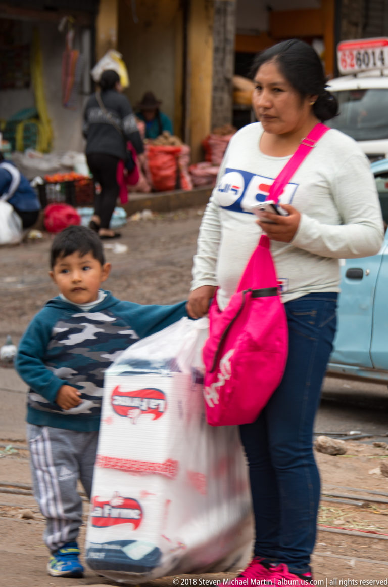 Woman carrying shopping bags and holding a young child's hand while walking beside railway tracks.