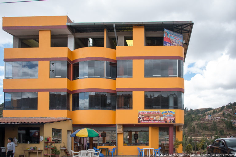 Bright orange multi-story commercial building with curved glass windows, restaurant signage, outdoor tables, and umbrella.