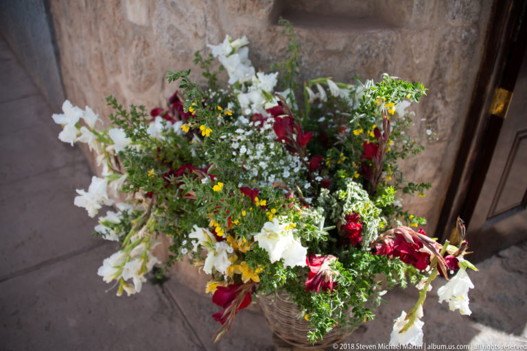 Mixed bouquet of white, red, and yellow flowers with green foliage arranged in a woven container.