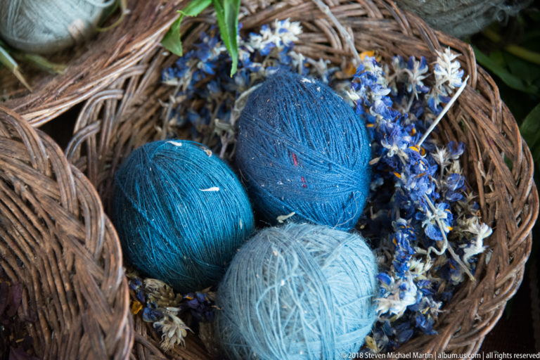 Turquoise, deep blue, and pale blue yarn balls arranged among small blue-and-white flowering material in a basket.