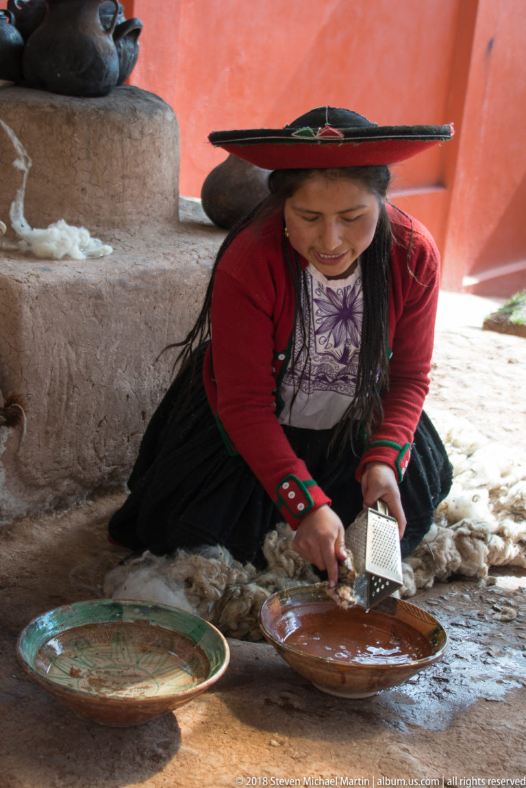 Woman in red highland clothing kneeling beside wool fleece while grating material over a shallow earthenware dish.