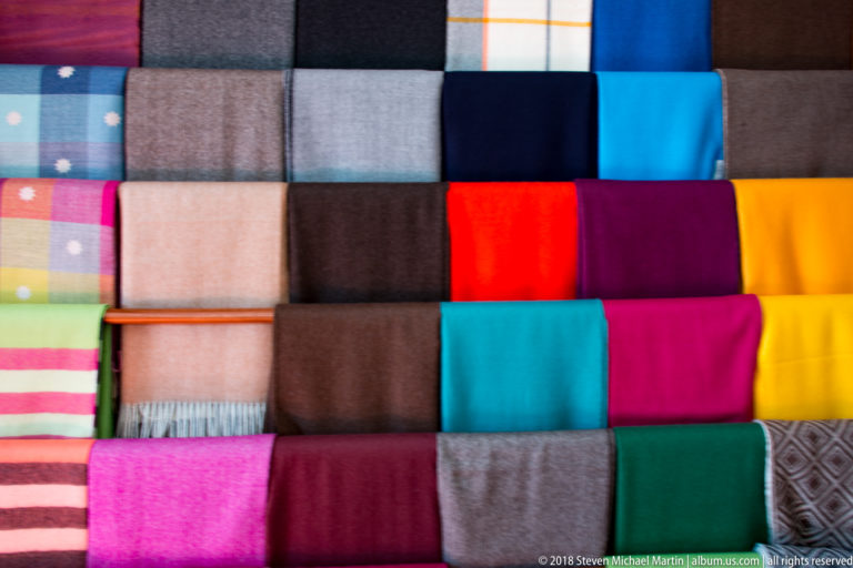 Grid of folded woven textiles in turquoise, magenta, yellow, red, green, gray, brown, black, and striped patterns.
