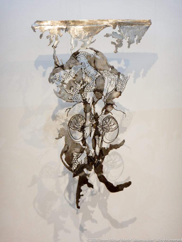 Intricate openwork wall sculpture of circular, mesh-like, and organic forms casting layered shadows on a white wall.