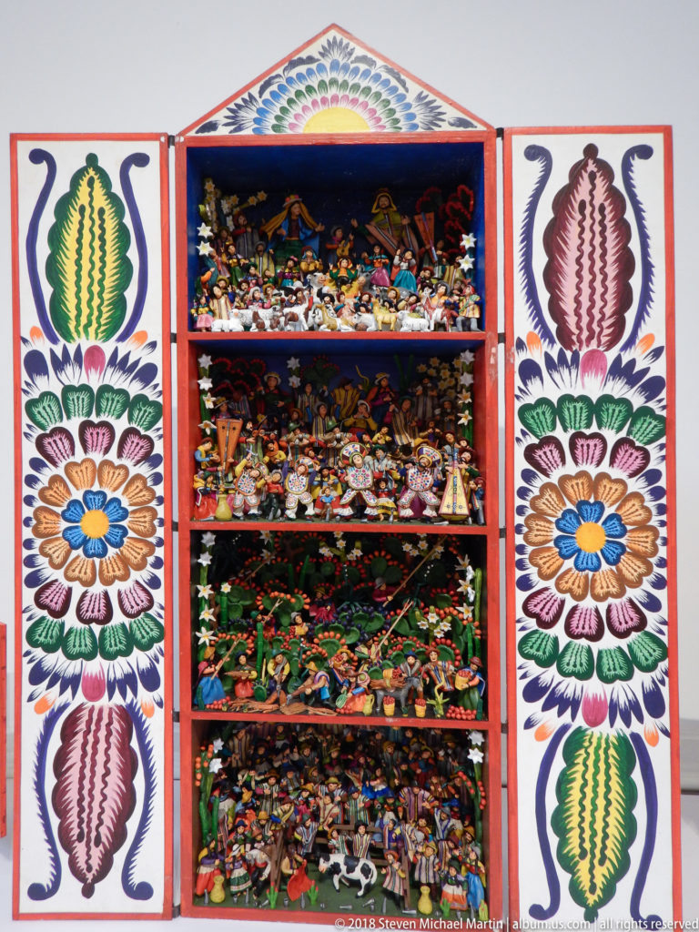 Tall open retablo with four crowded miniature tiers and doors painted with vertical rows of large flowers and leaves.