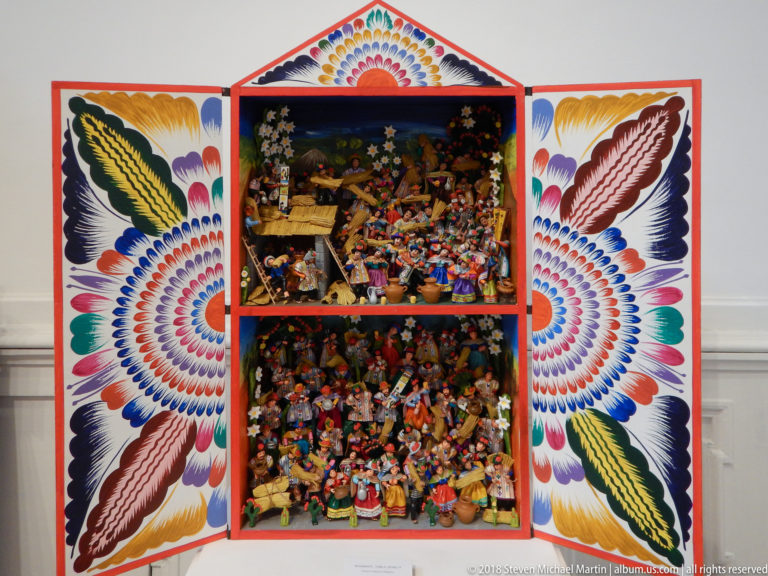 Open two-tier retablo densely packed with tiny colorful figures, animals, and objects, framed by large painted floral doors.