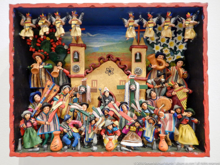 Colorful relief with a twin-towered church surrounded by musicians, dancers, and festival figures beneath a painted sky.