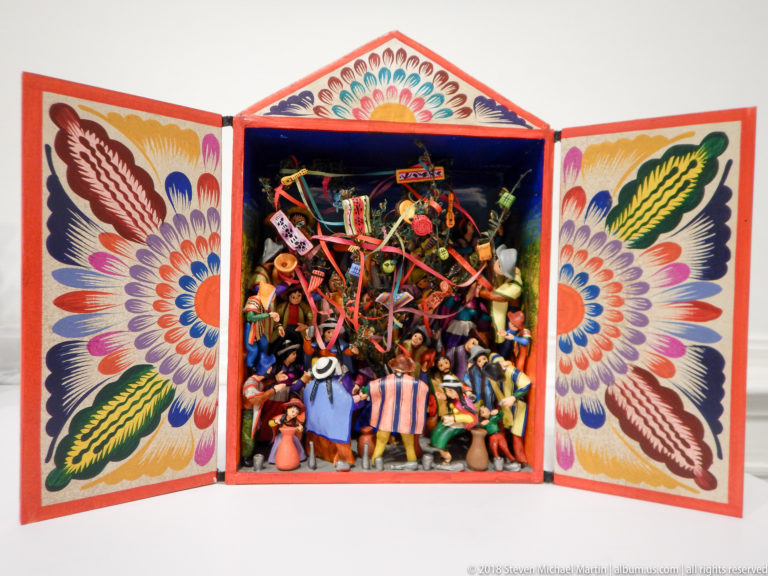 Open painted retablo filled with miniature musicians, dancers, animals, and festival figures, with floral designs across both doors.