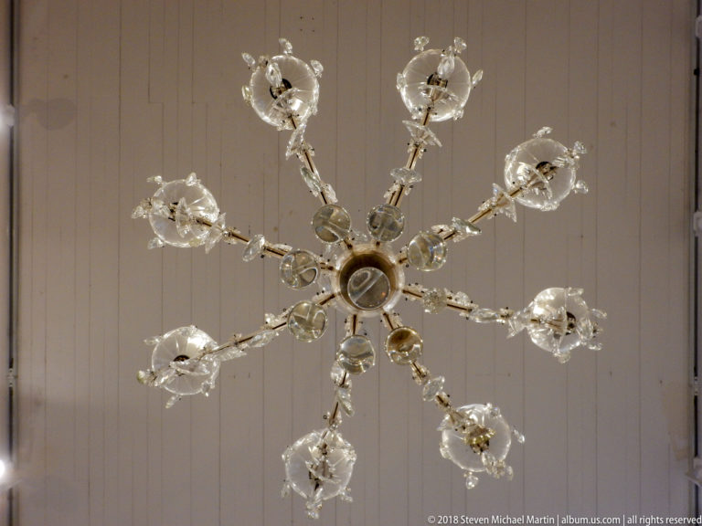 Cut-glass chandelier viewed from directly below, with radiating arms, flower-shaped cups, and faceted pendants.