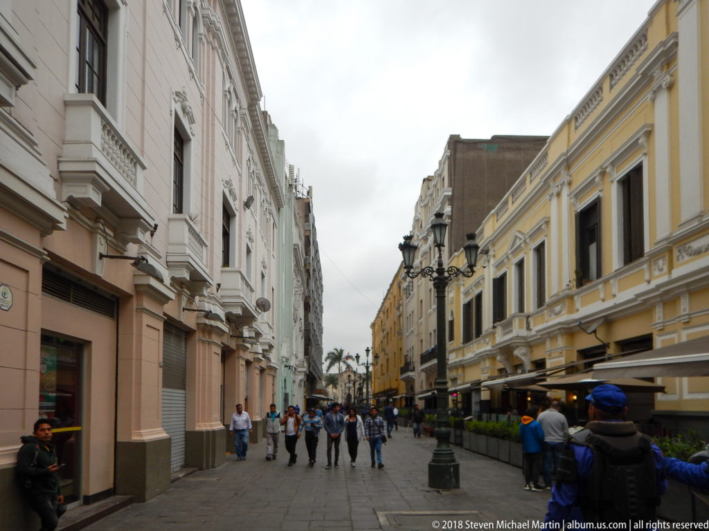 Pedestrians walking along a central Lima street between restored white, blue, and yellow historic façades.