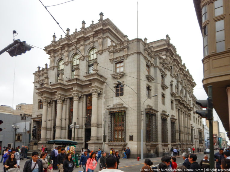 Ornate pale stone corner building with giant columns and tall windows above a crowded Lima intersection.